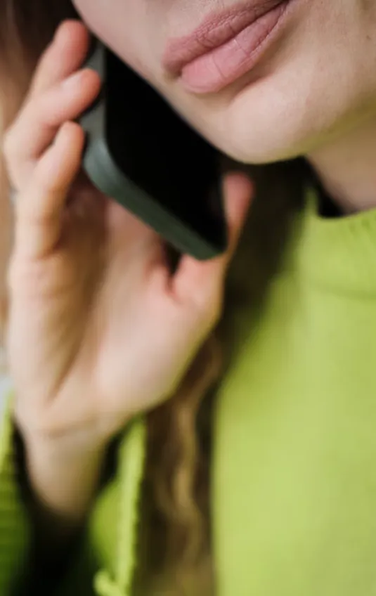 Close-up of a person holding a black smartphone to their ear, wearing a green sweater.