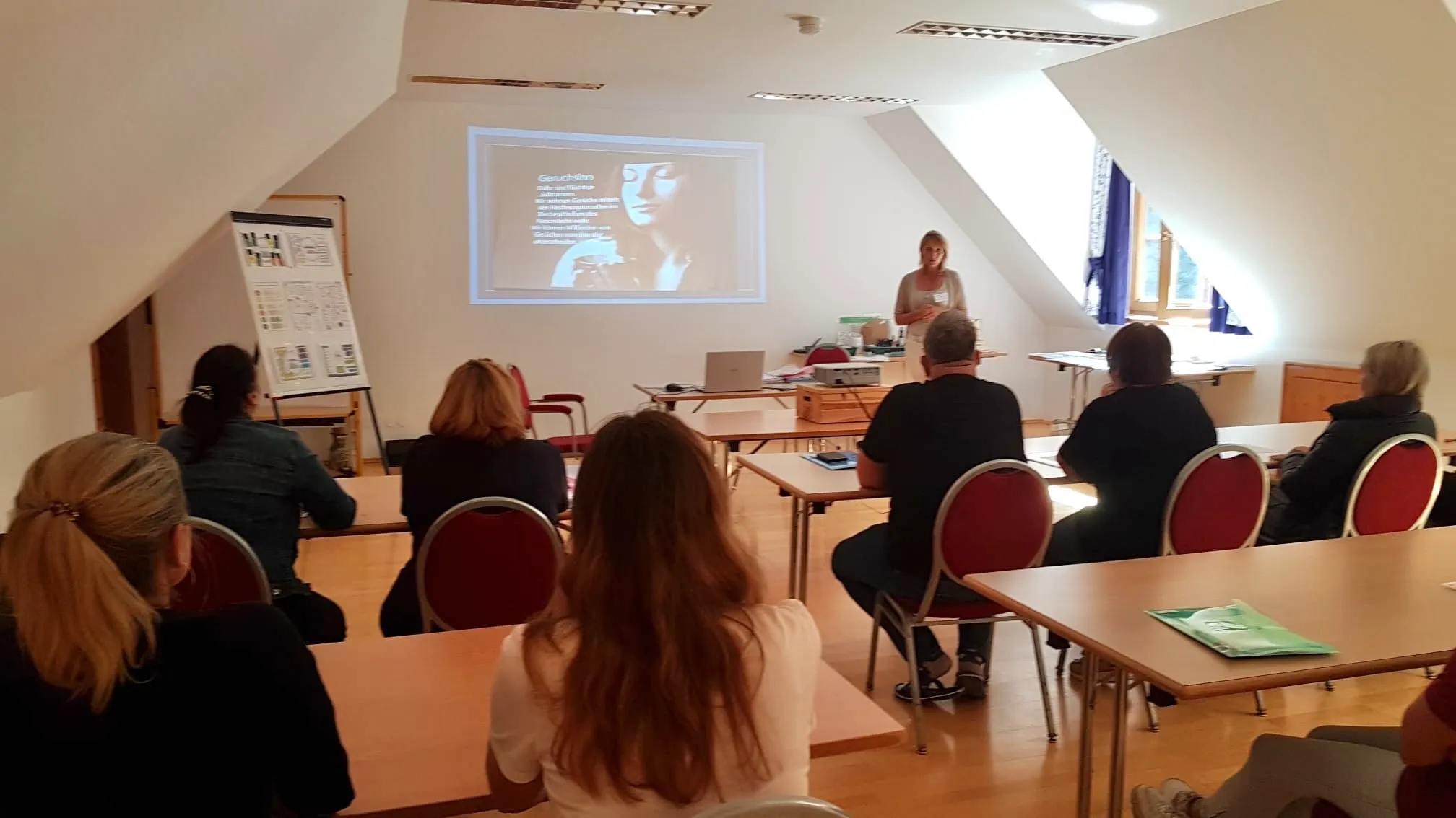 Lisa Walder hält eine Aroma-Präsentation in einem hellen Raum vor einem Publikum, mit einer Projektion an der Wand und mehreren Personen, die an Tischen sitzen.