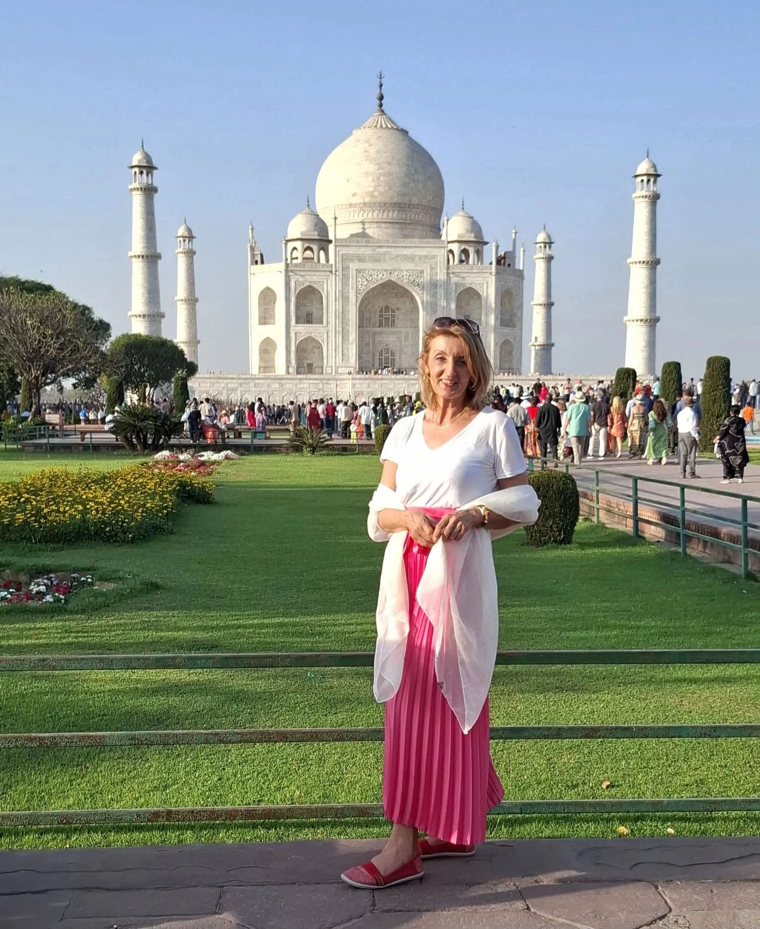 Lisa Walder mit weißem Oberteil und pinkem Rock vor dem Taj Mahal in Indien bei sonnigem Himmel.