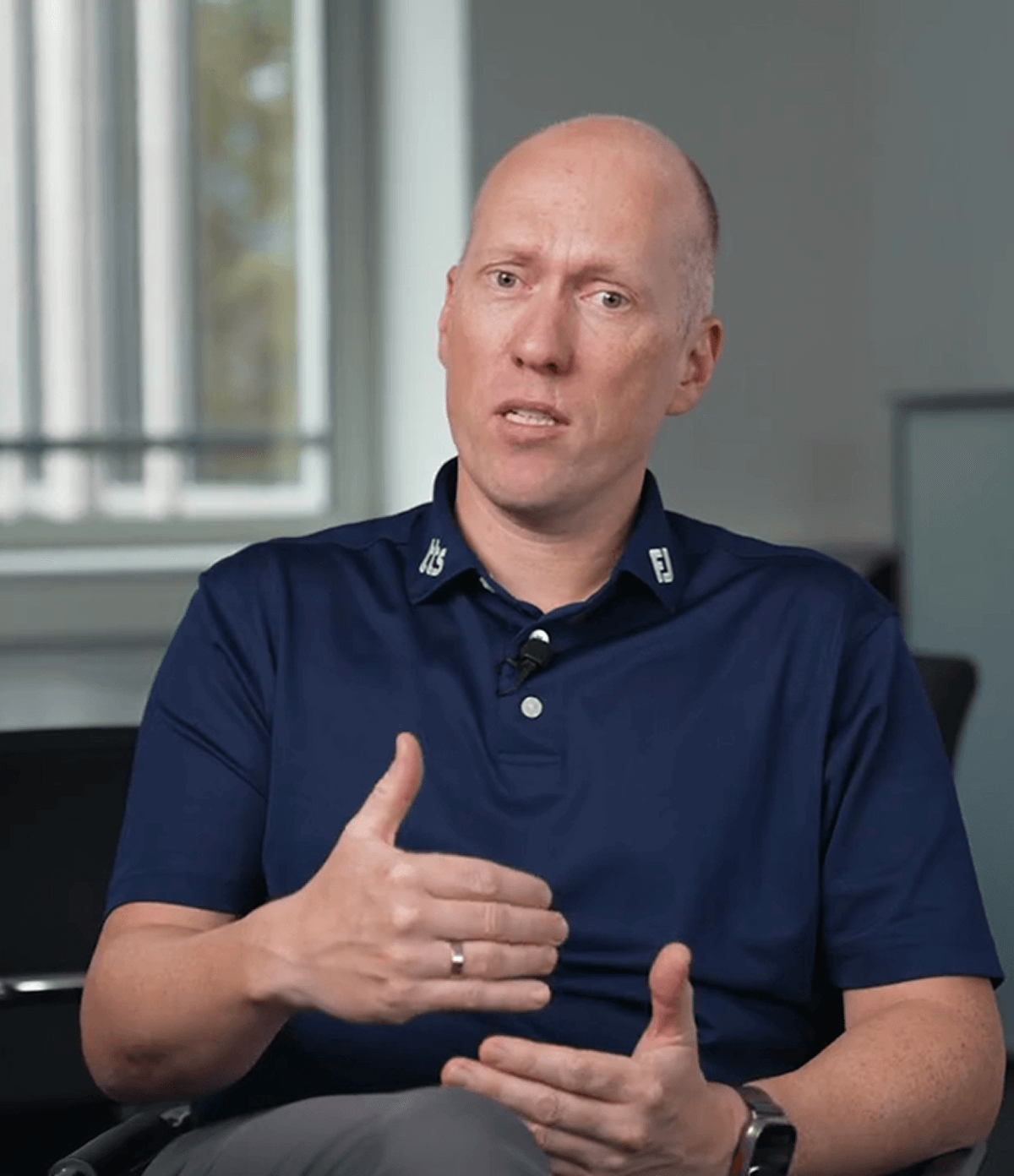 Lächelnder Mann in blauem Hemd sitzt an modernem Büroschreibtisch mit Laptop im Hintergrund.