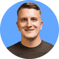 Ein lächelnder Mann mit kurzem Haar und dunkelgrauem T-Shirt vor blauem Hintergrund.