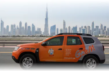 Orange and gray GeeM branded SUV parked with Dubai skyline and Burj Khalifa in the background.