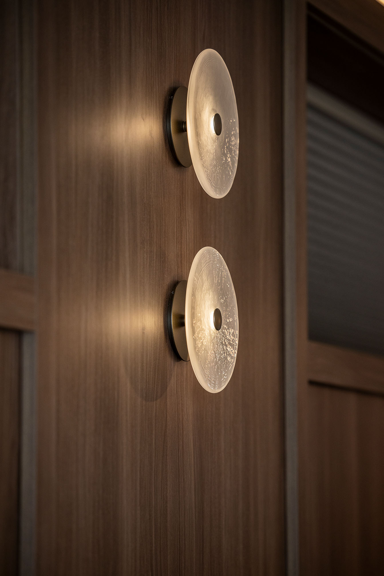 Two round wall sconces with textured glass shades mounted on a wood-paneled wall.