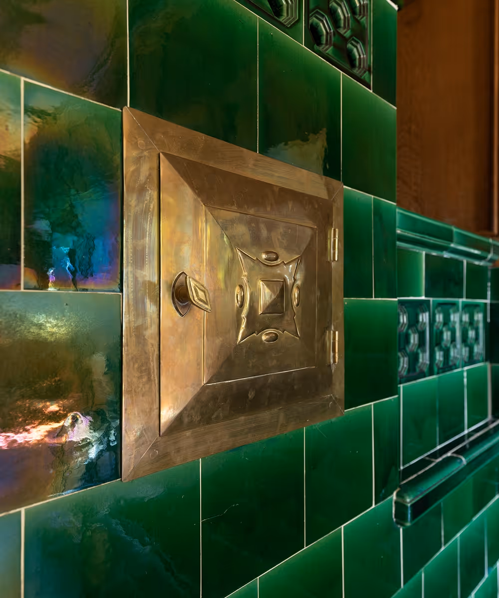 Bronzetür mit dekorativem Muster eingebettet in grüne, glasierten Fliesenwand.