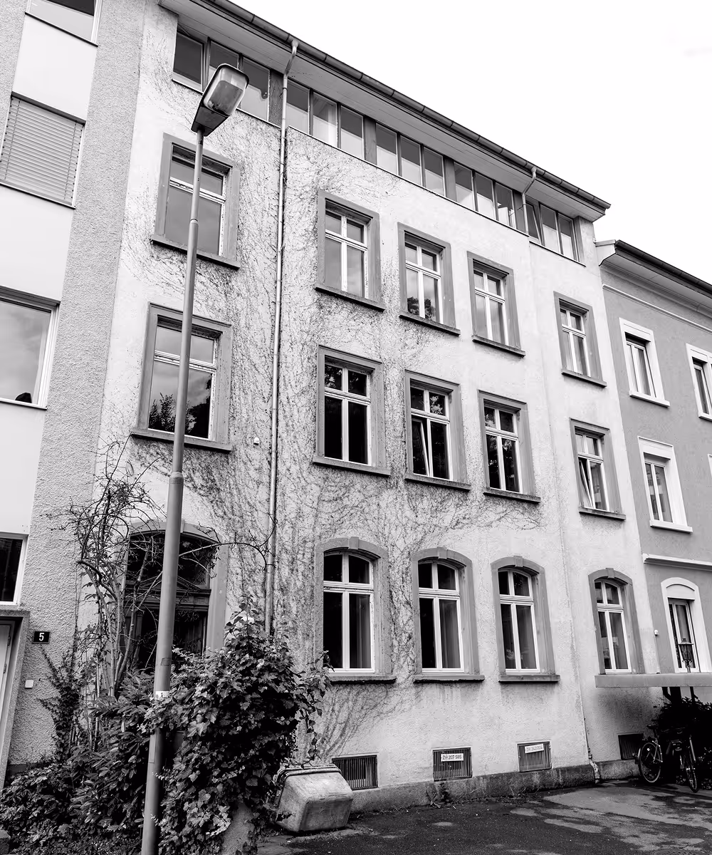 Schwarz-Weiss-Bild eines mehrstöckigen Wohngebäudes mit alten Fenstern und einer Laterne davor.