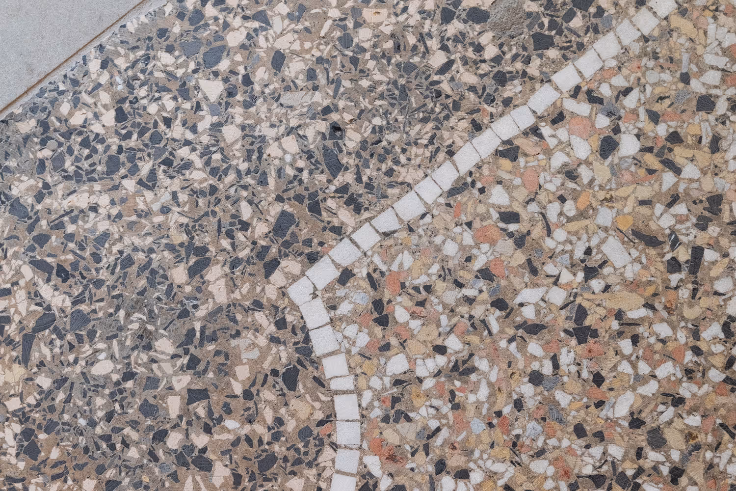 Nahaufnahme eines Terrazzo-Bodenbelags mit farbigen Steinchen und weißen Mosaiklinien.