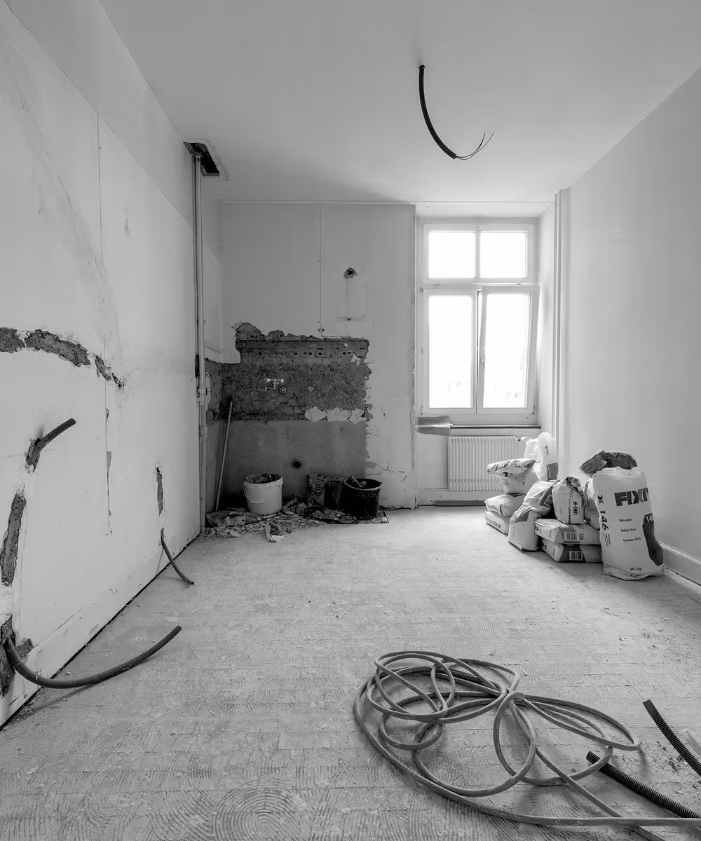 Renovationsraum mit unverputzten Wänden, Bauutensilien und -materialien vor einem Fenster.