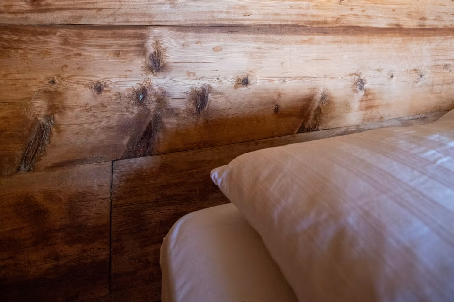 Nahaufnahme eines Holzbettkopfteils mit sichtbaren Holzmaserungen und einem weißen Kissen daneben.