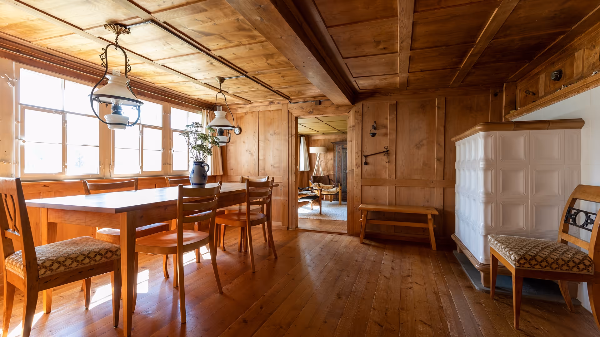 Rustikaler Essbereich mit Holztisch, Stühlen und großen Fenstern in einem gemütlichen Chalet mit Kachelofen.