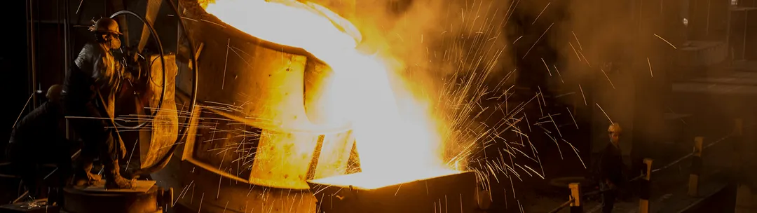 A large industrial furnace pouring molten metal, with sparks flying around in a dark, high-heat environment.