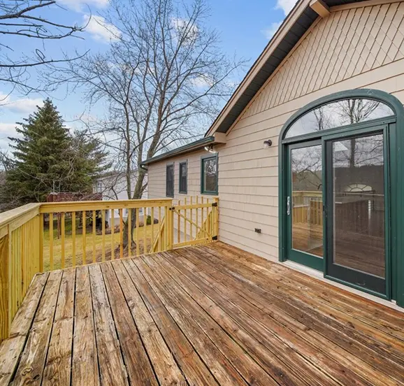 Wooden deck attached to beige house with green-framed sliding glass door, overlooking leafless trees and a grassy yard. | Metrex Equities