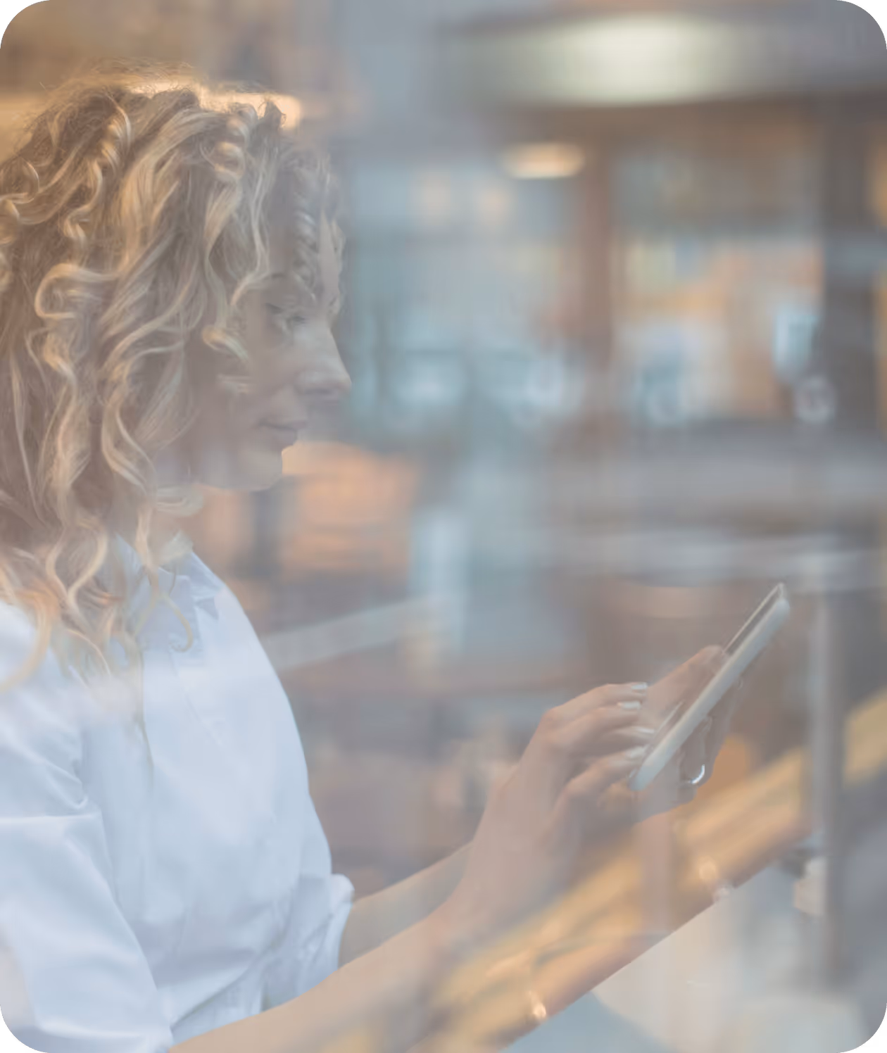 Woman with curly hair using a smartphone, viewed through a window with reflections.