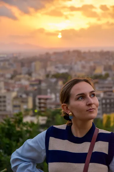 Young woman with striped sweater and earrings looks up at sunset over a cityscape background.