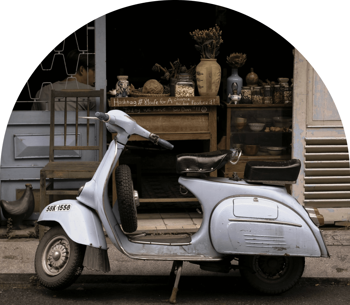 Light blue vintage scooter parked in front of a shop with decorative jars and wooden furniture.
