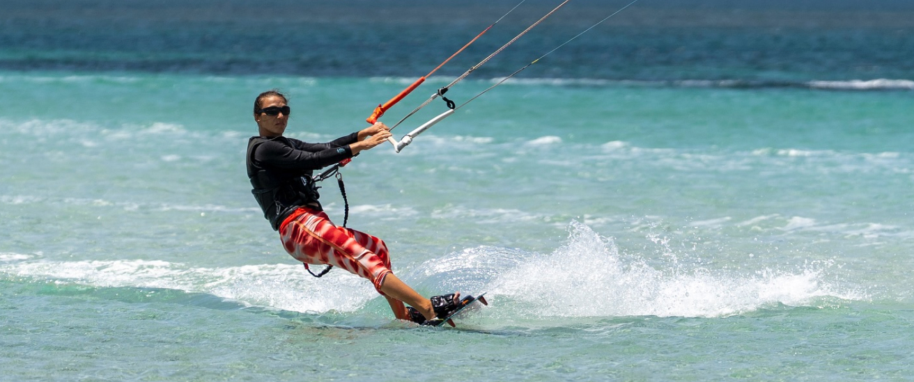 Person kiteboarding on turquoise water wearing sunglasses and red patterned pants.