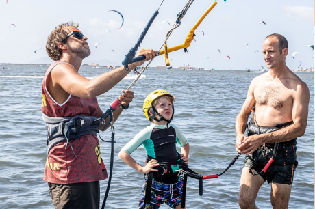 Two men and a child in the water prepare for kiteboarding, holding the kite control bar and lines.