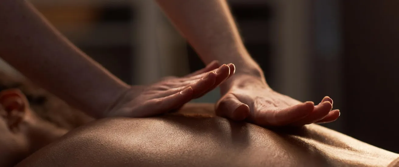 Hands giving a relaxing back massage to a person lying face down in soft lighting.