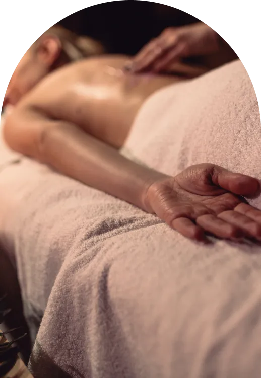 Person lying face down on a towel-covered surface receiving a back massage with oil.