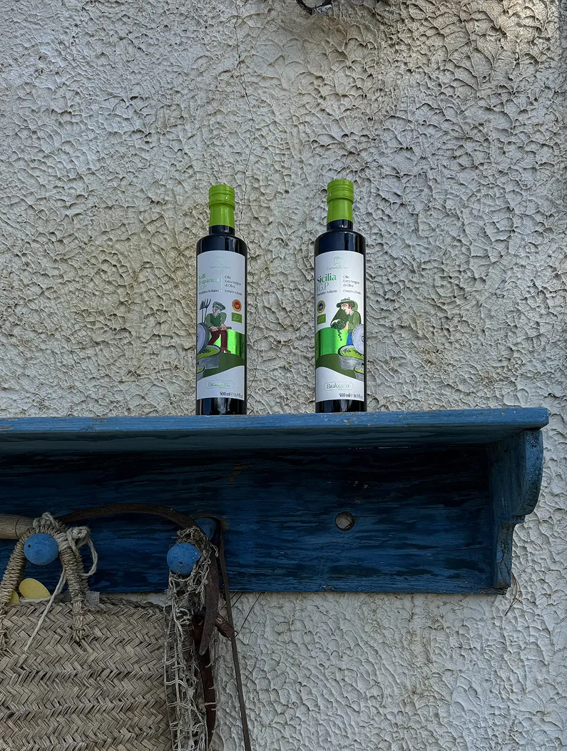 Two bottles of olive oil with green caps on a blue wooden shelf against a textured wall.