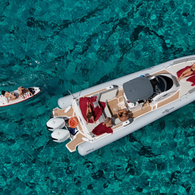 People relaxing on a white motorboat and a person paddling nearby on clear turquoise water.
