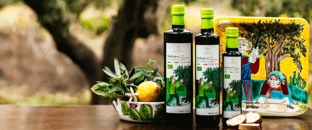 Three bottles of Italian Biologico olive oil with lemon and bread on a wooden table with decorative ceramic items.