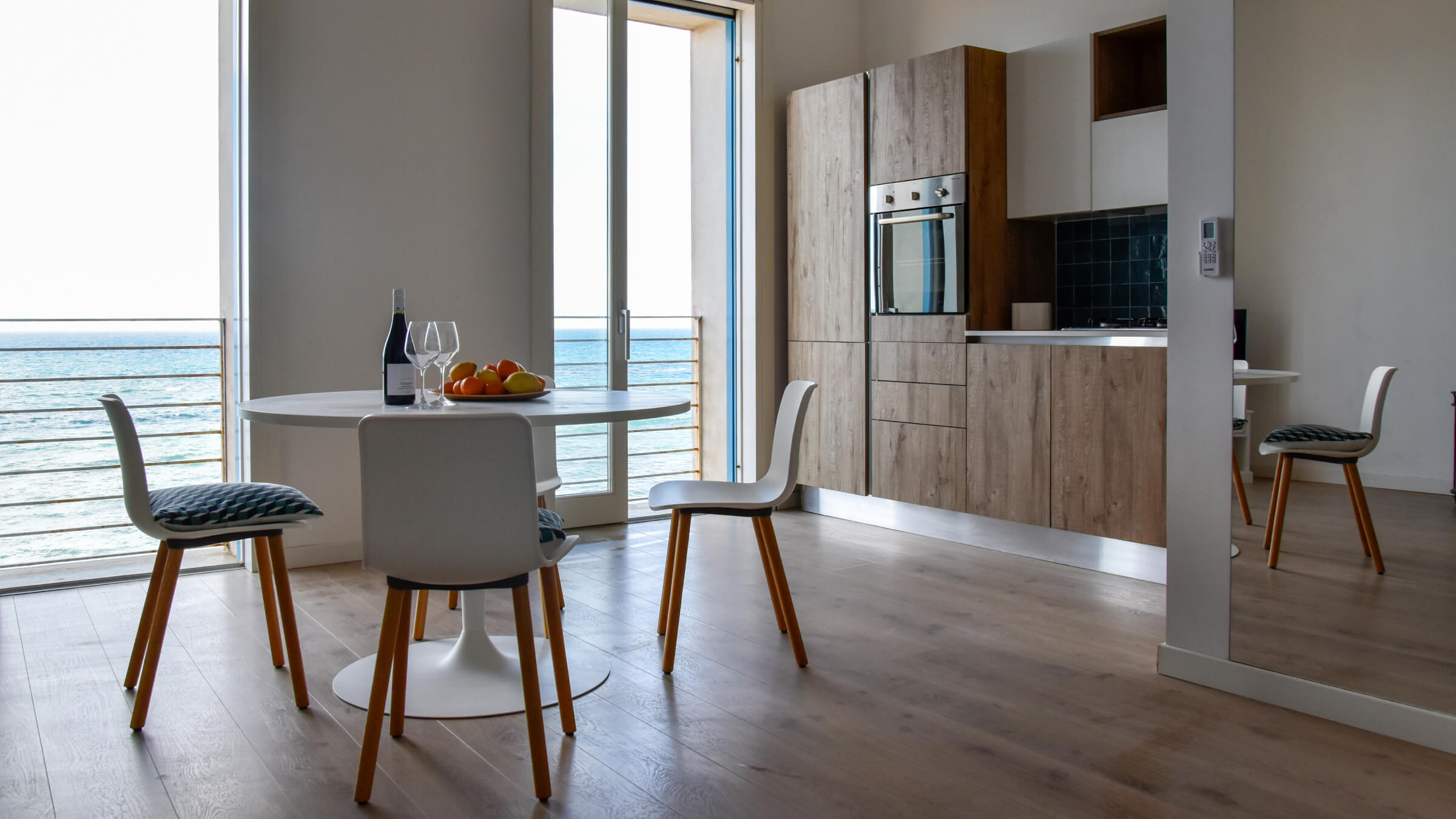 Jasny salon z aneksem kuchennym i stołem jadalnianym w apartamencie Seaside w Trapani, z dużymi oknami i widokiem na morze
