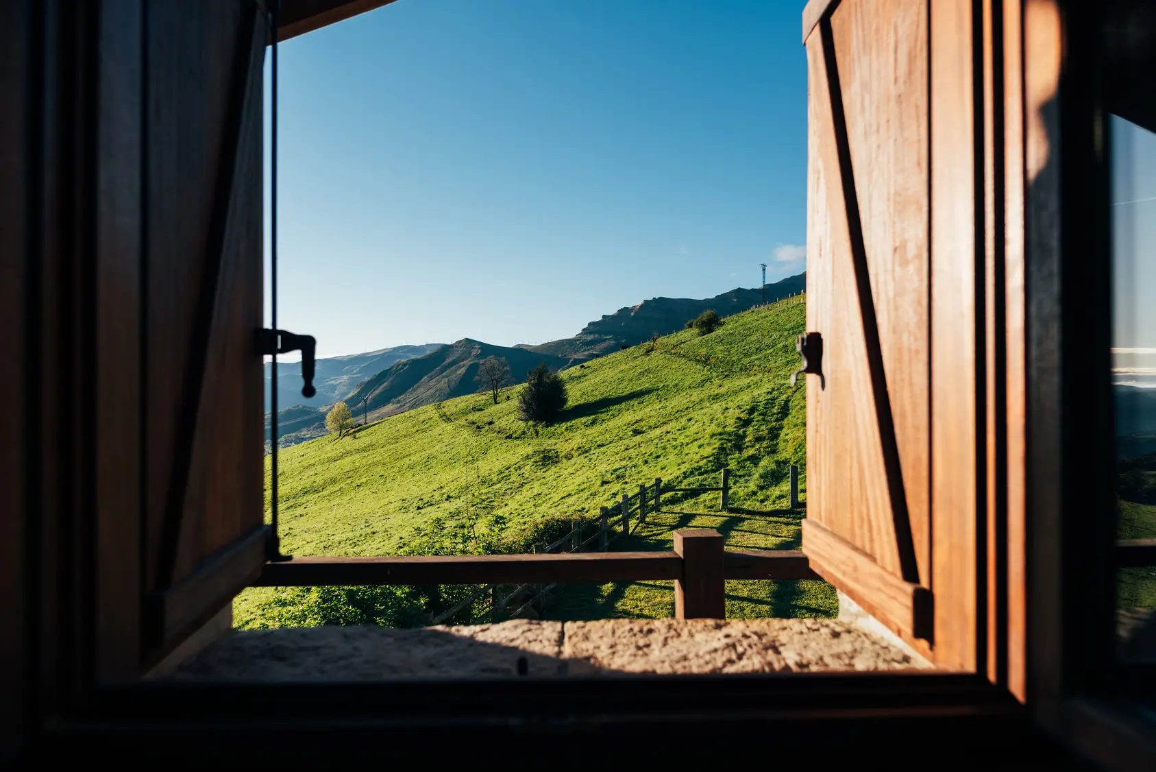 View of green hillside and distant mountains through an open wooden window.
