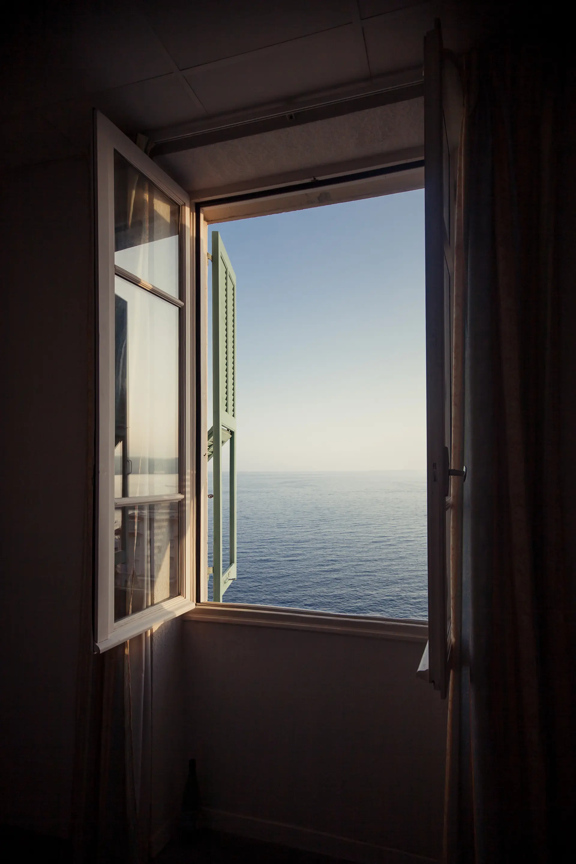 Open window overlooking calm sea under clear sky at dusk or dawn.