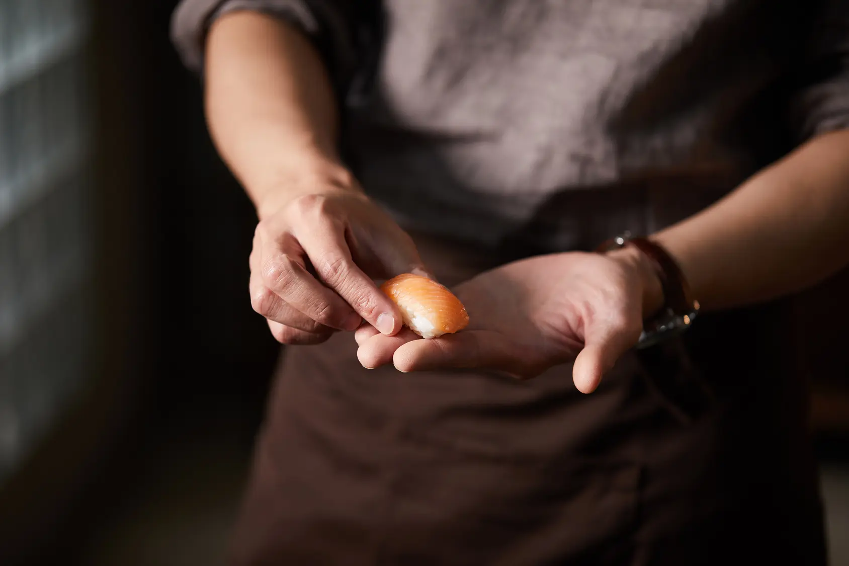 Person holding a piece of salmon nigiri sushi between their fingers over an open palm.