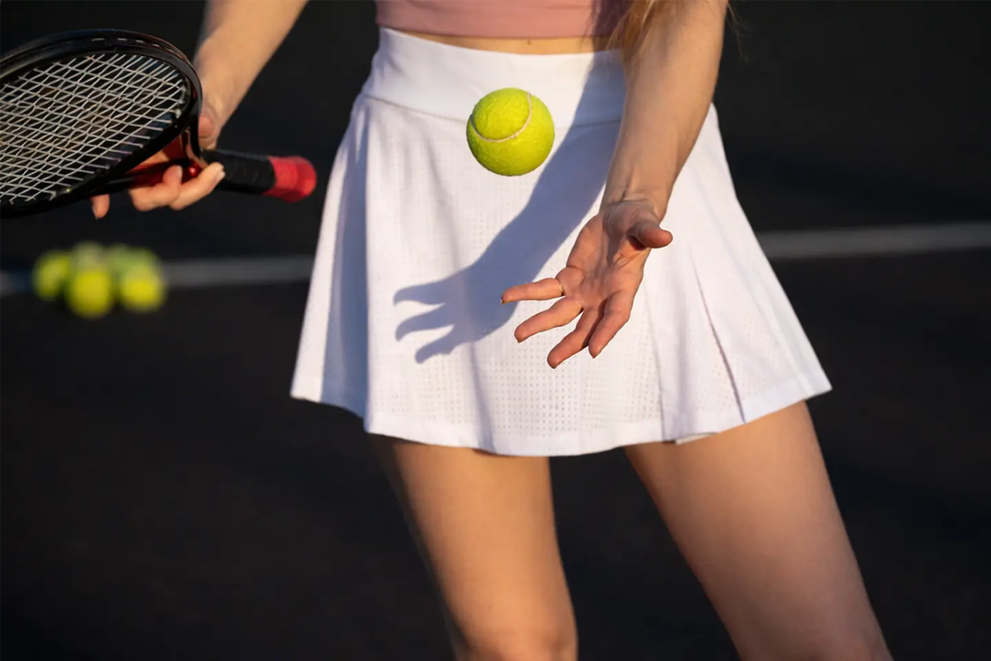 Close-up of a tennis player tossing a tennis ball before a serve, wearing a white skirt and holding a racket.
