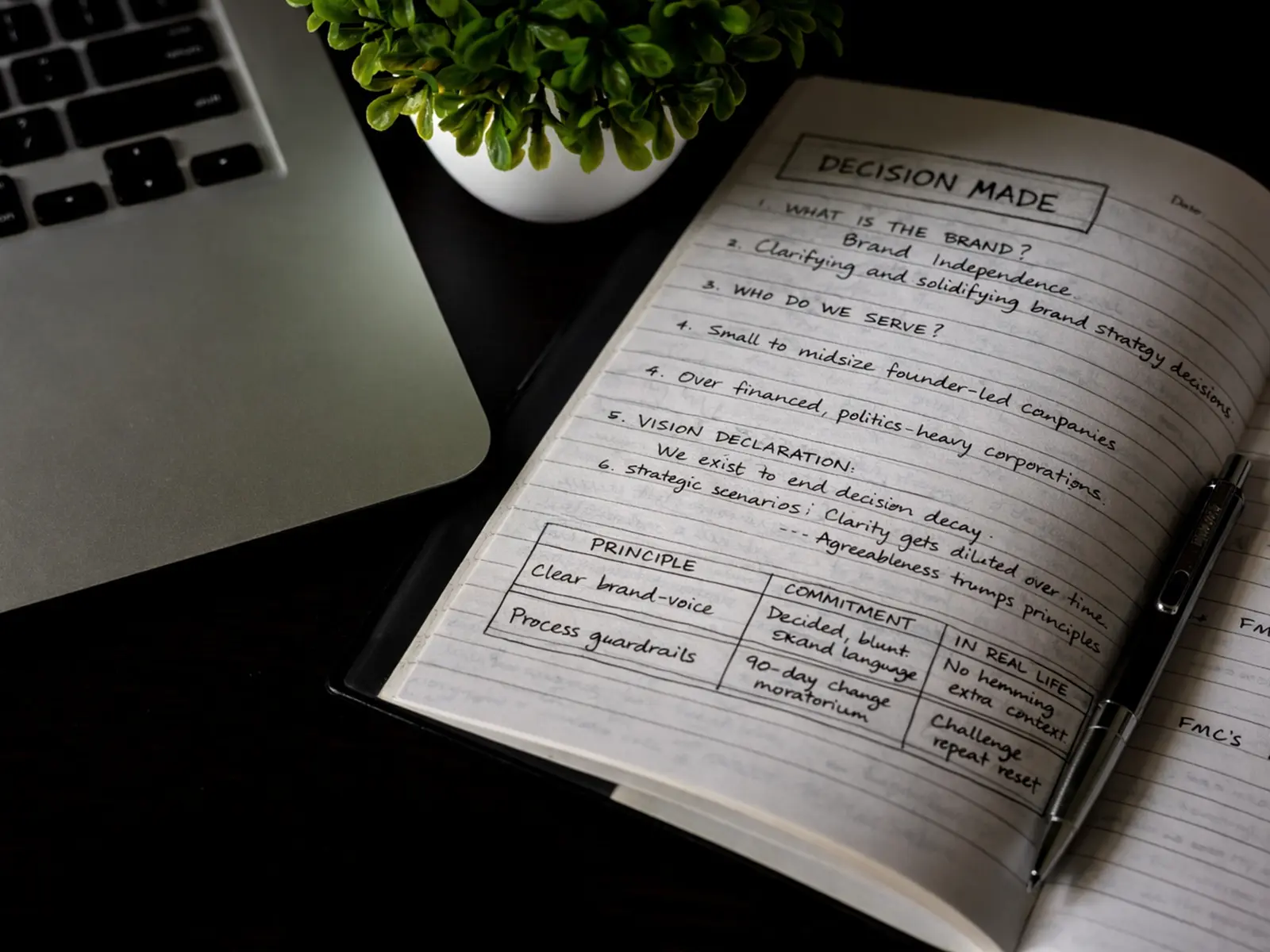 Open notebook on a desk with handwritten notes titled 'Decision Made,' next to a laptop and a pen.