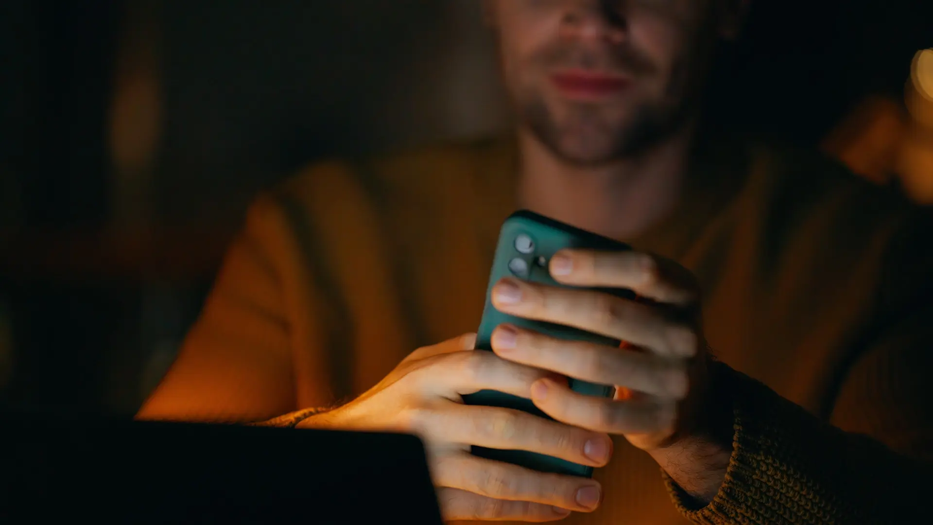 Person holding a smartphone in both hands in a dimly lit environment.
