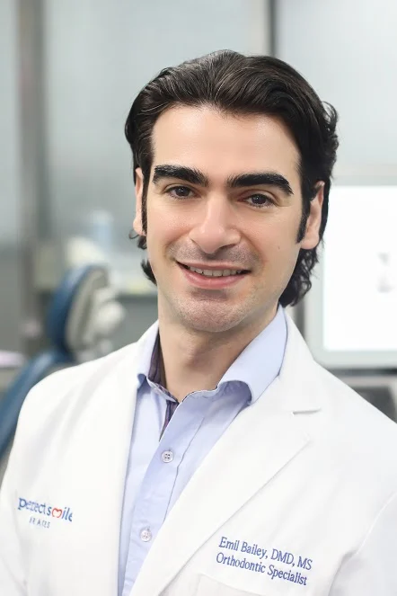Professional portrait of Dr. Emil Bailey, founder of Perfect Smile Doc, showing his dentist's coat and the confidence he inspires in his patients.