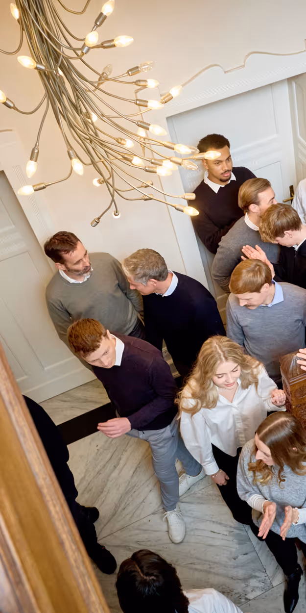 Group of people gathered indoors on a marble floor under a modern chandelier with exposed bulbs.