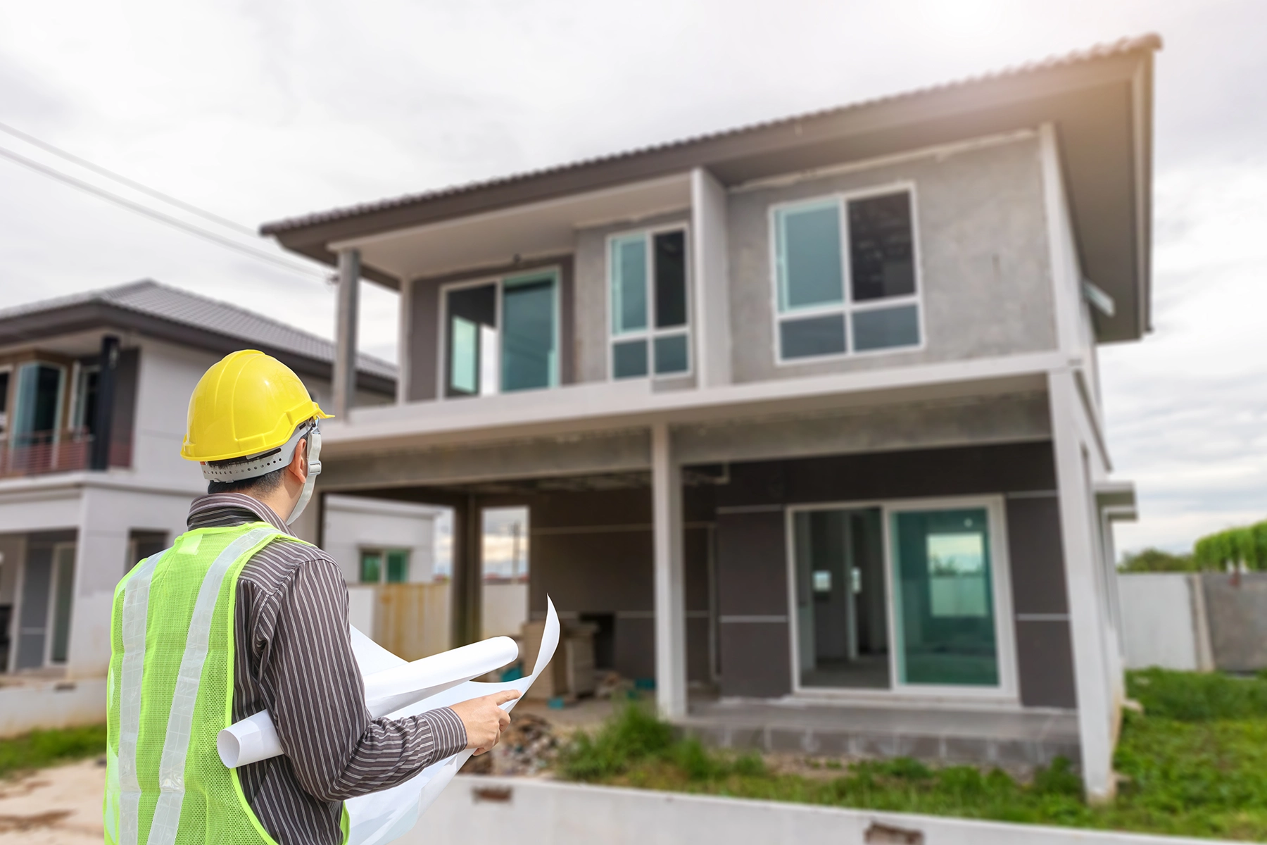 Inspector wearing safety gear reviewing plans in front of a recently repaired home, representing Peak Pro Home Services’ $99 post-repair inspection for buyers and sellers.