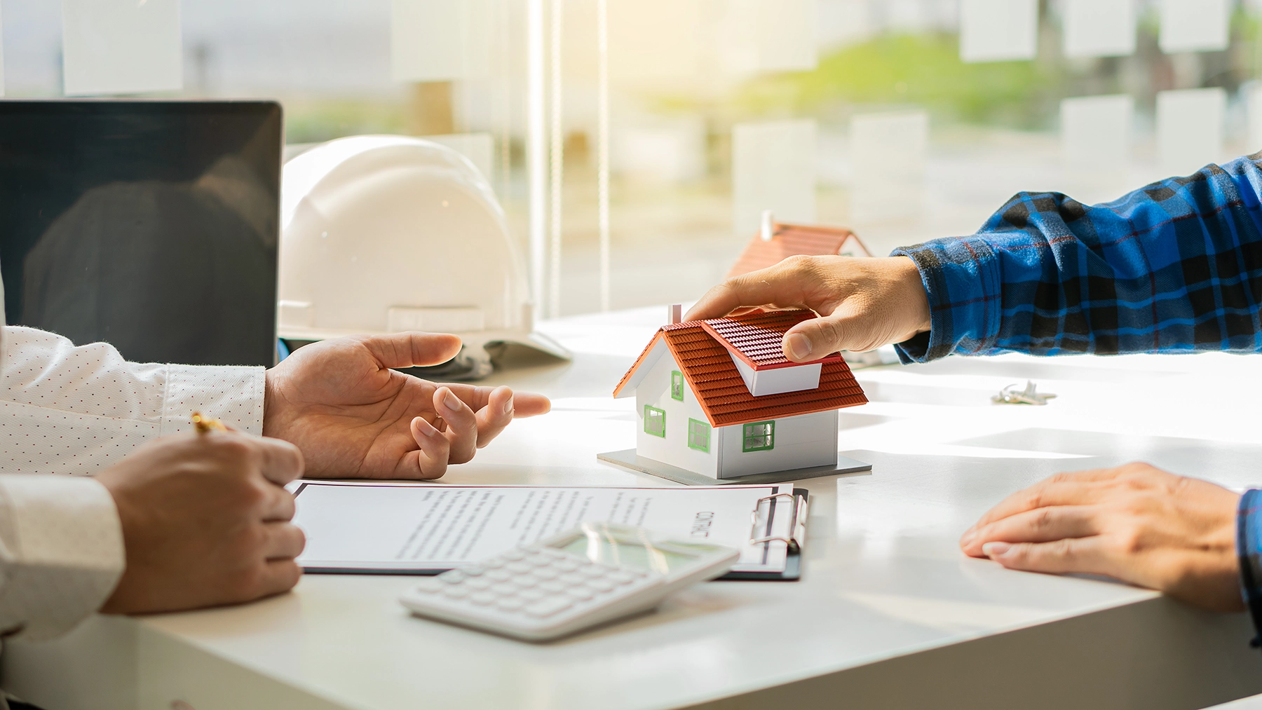 Landlord meeting with a home services professional while reviewing property documents and a house model, representing Peak Pro Home Services’ support for landlords and rental property maintenance.