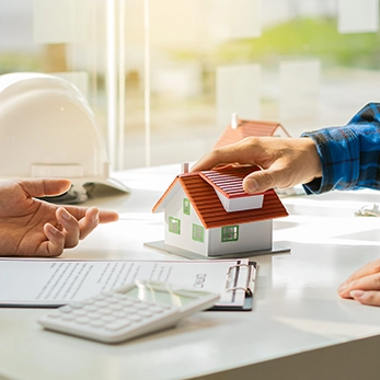 Landlord meeting with a home services professional while reviewing property documents and a house model, representing Peak Pro Home Services’ support for landlords and rental property maintenance.