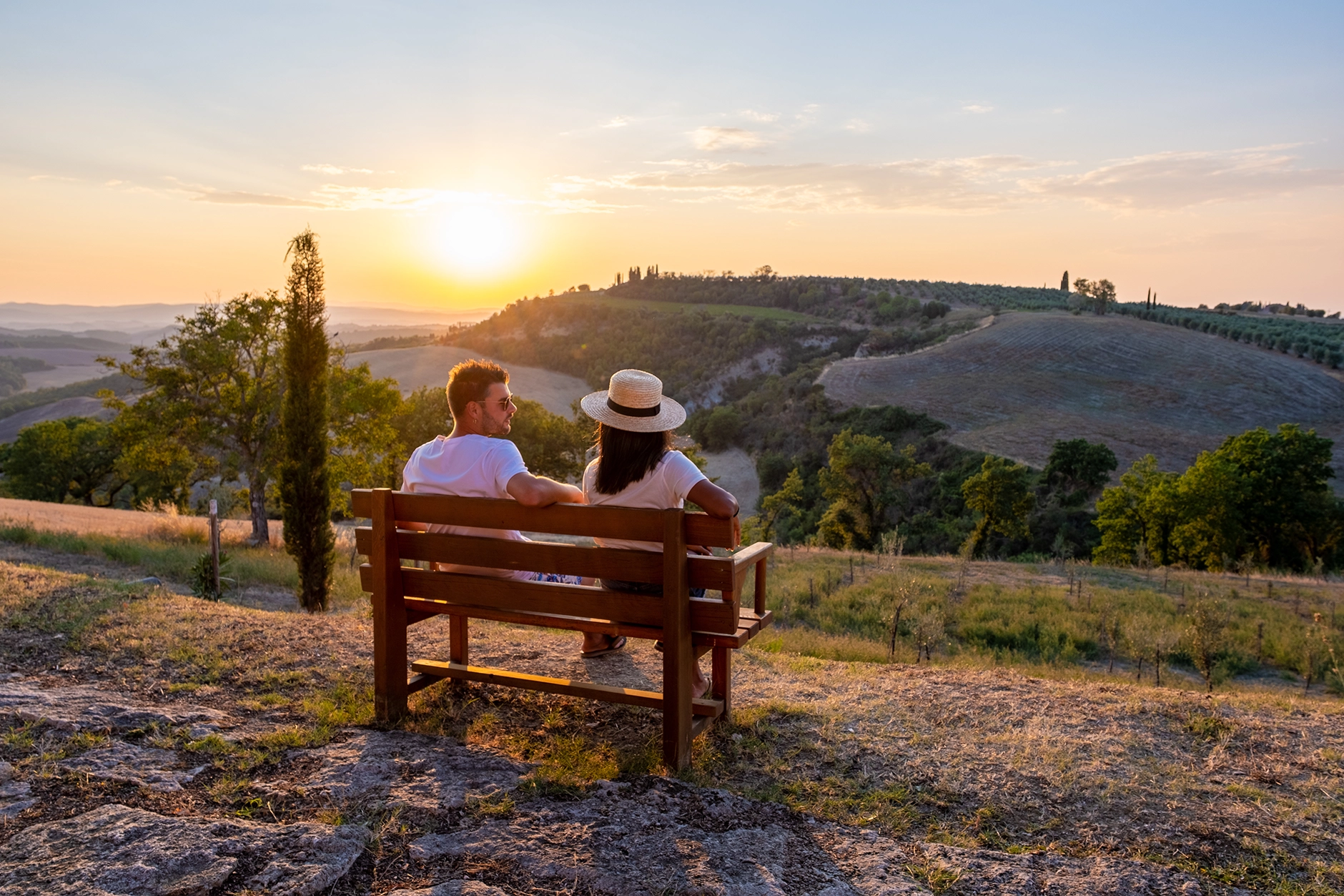 Couple sitting on a wooden bench overlooking rolling hills and farmland at sunset, representing the rural landscape of Gleed, Yakima County, Washington.