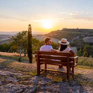 Couple sitting on a wooden bench overlooking rolling hills and farmland at sunset, representing the rural landscape of Gleed, Yakima County, Washington.