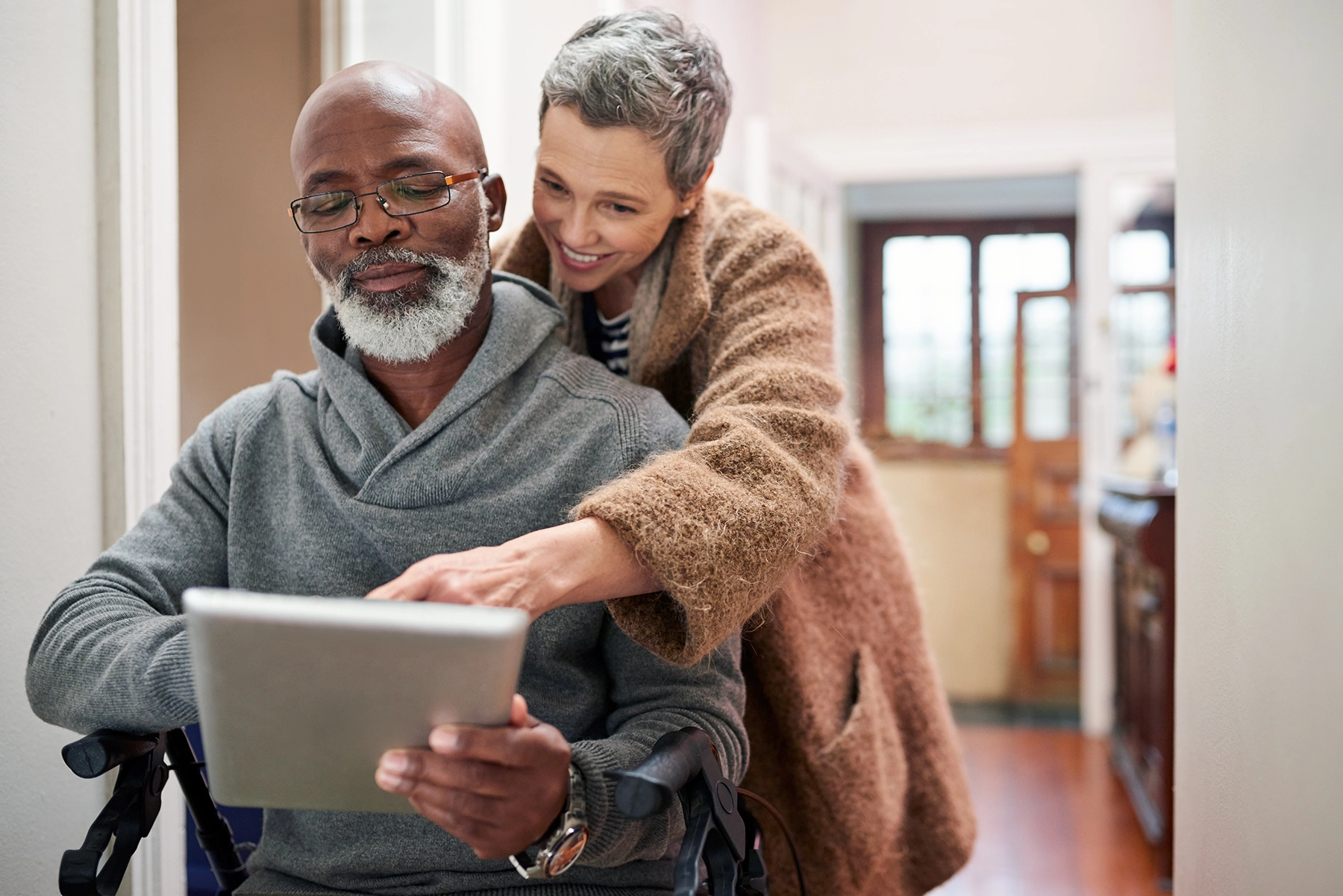 A woman assisting a senior man in a wheelchair while they look at a tablet, illustrating how Peak Pro Home Services supports mobility needs and accessibility planning for Yakima seniors.