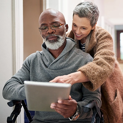 A woman assisting a senior man in a wheelchair while they look at a tablet, illustrating how Peak Pro Home Services supports mobility needs and accessibility planning for Yakima seniors.