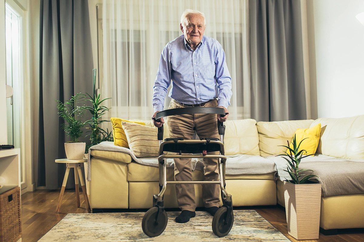 Older man using a walker in a well-lit living room with clear walking paths.