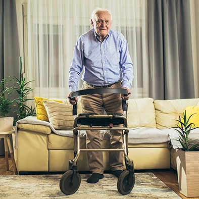 Older man using a walker in a well-lit living room with clear walking paths.