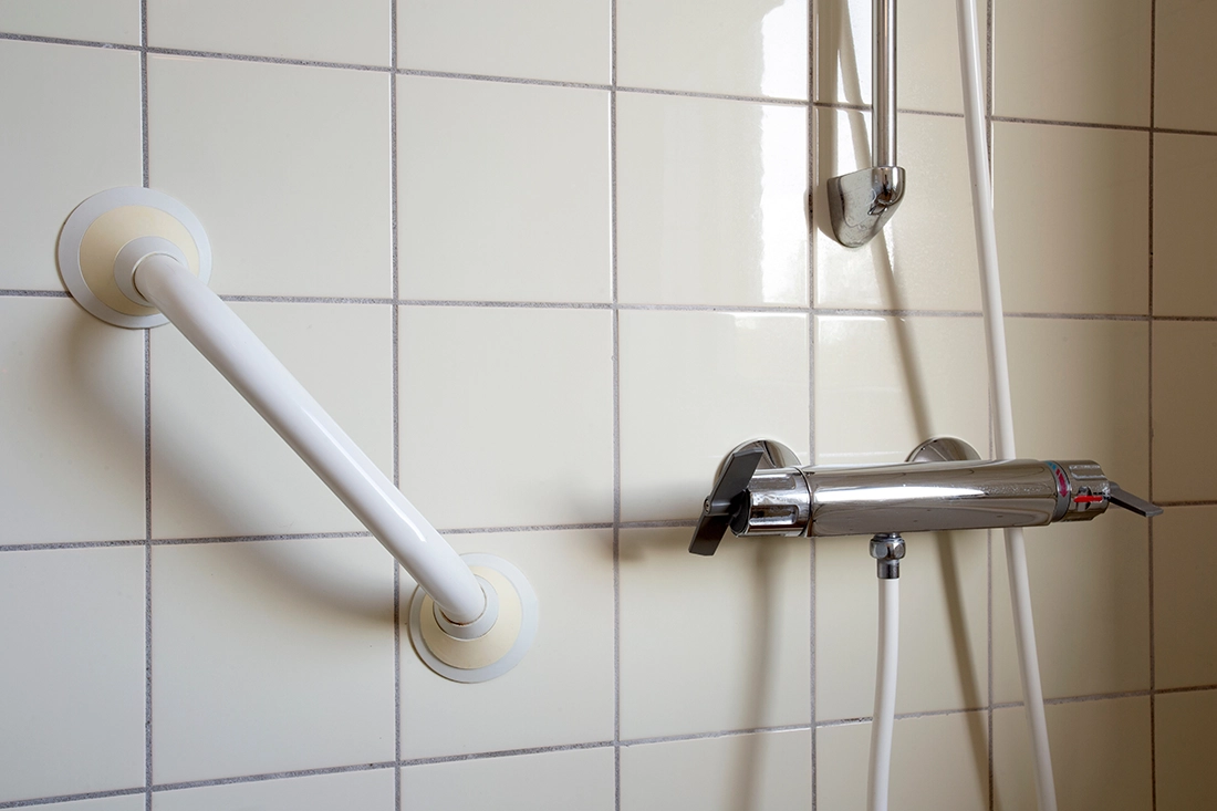 Close-up of a securely installed grab bar mounted on tiled shower wall next to a handheld shower fixture for added stability.