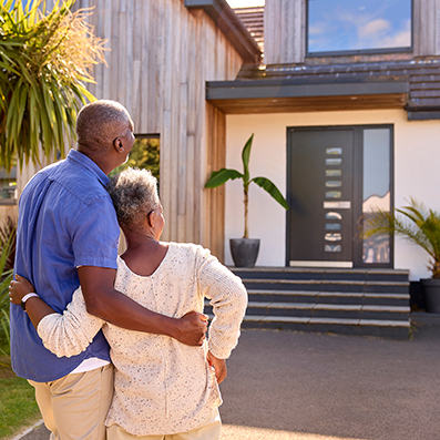 Older couple standing outside their modern home, representing proactive home maintenance planning and long-term home care in Yakima.