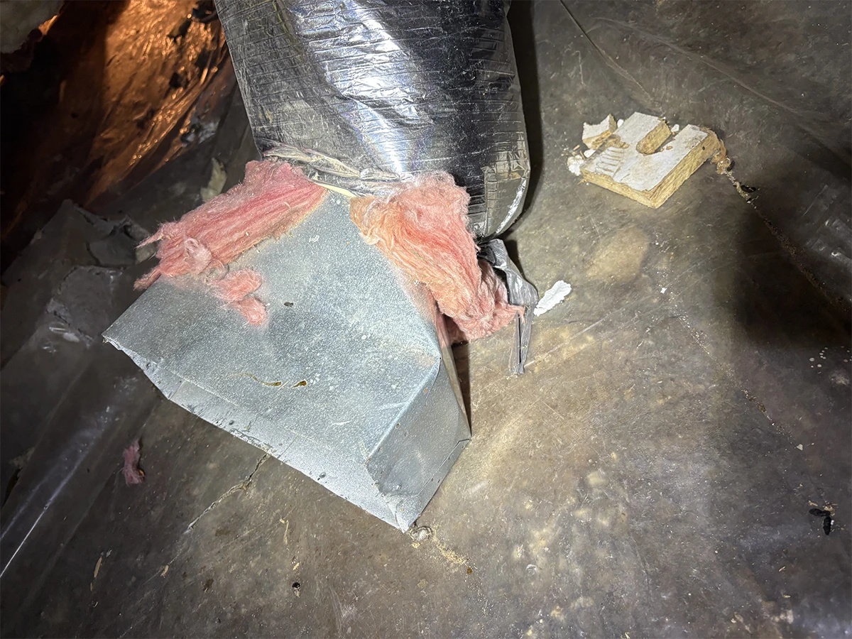 A disconnected HVAC duct left sitting on the crawl space floor with torn insulation, blowing conditioned air into the crawl space instead of into the home.