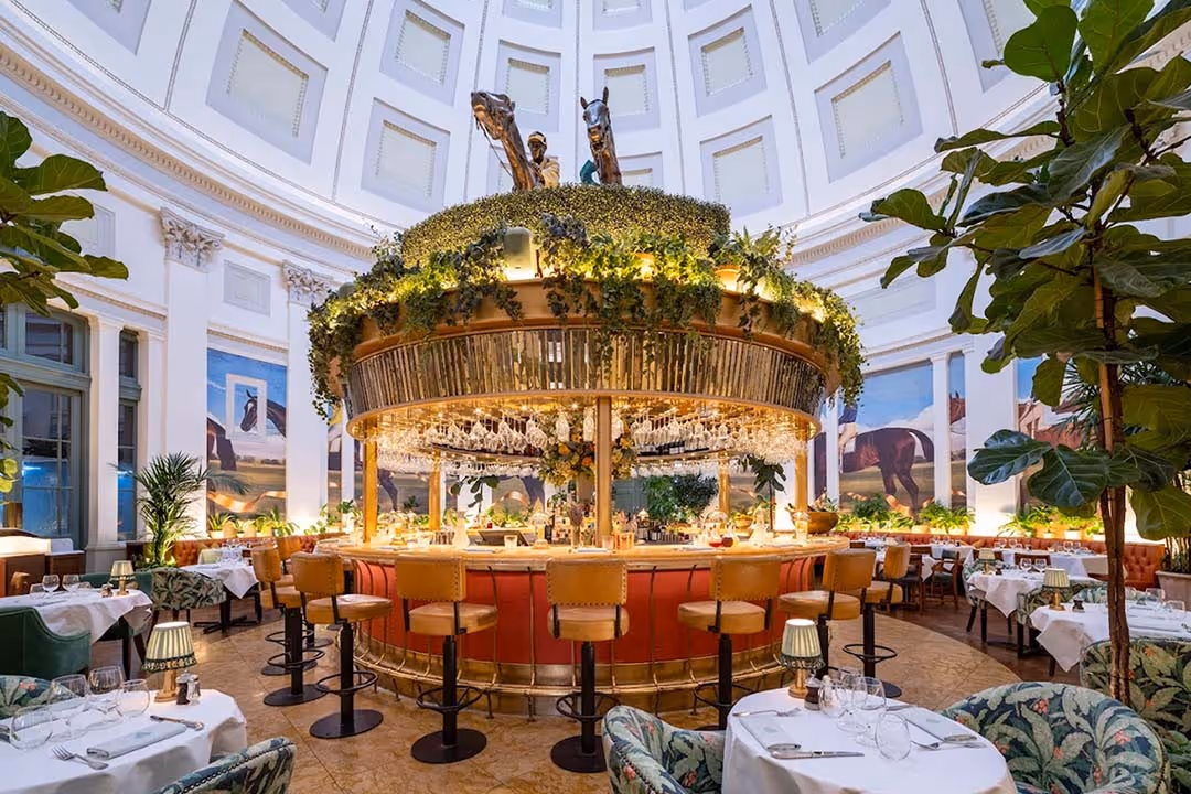 Elegant circular bar with hanging wine glasses and greenery centerpiece under a large white domed ceiling in a stylish restaurant.
