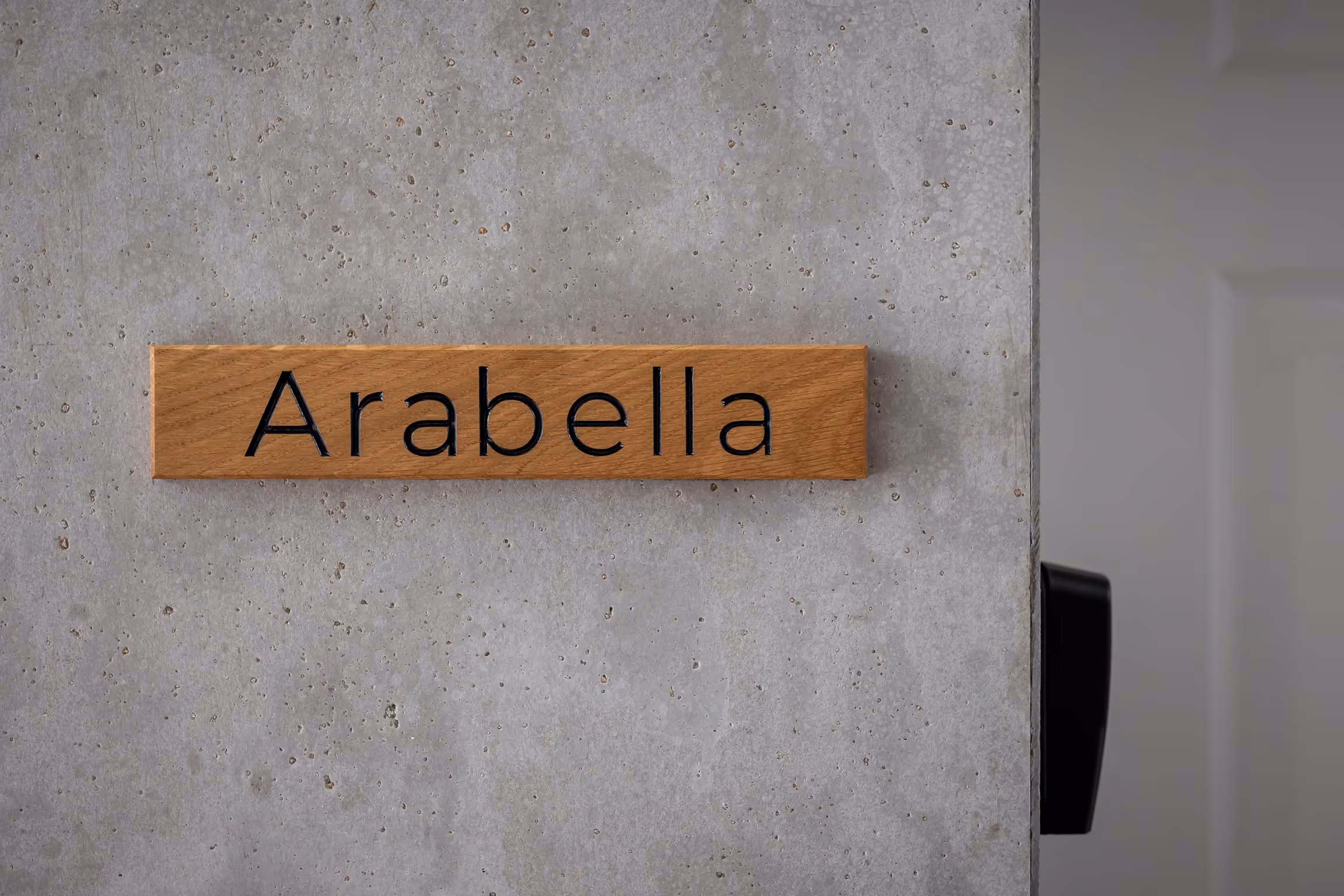 Wooden sign with the name 'Arabella' mounted on a concrete wall.