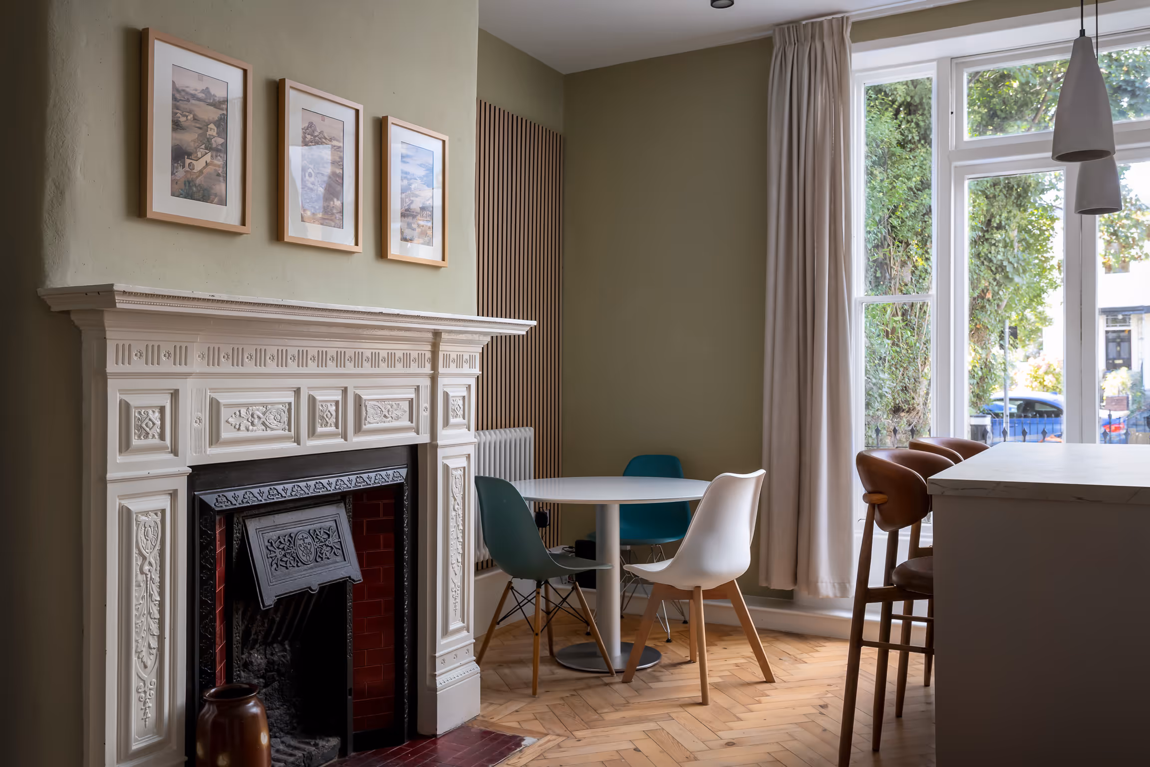 Cozy dining area with a white round table, three chairs, a decorative fireplace, and large window with beige curtains.