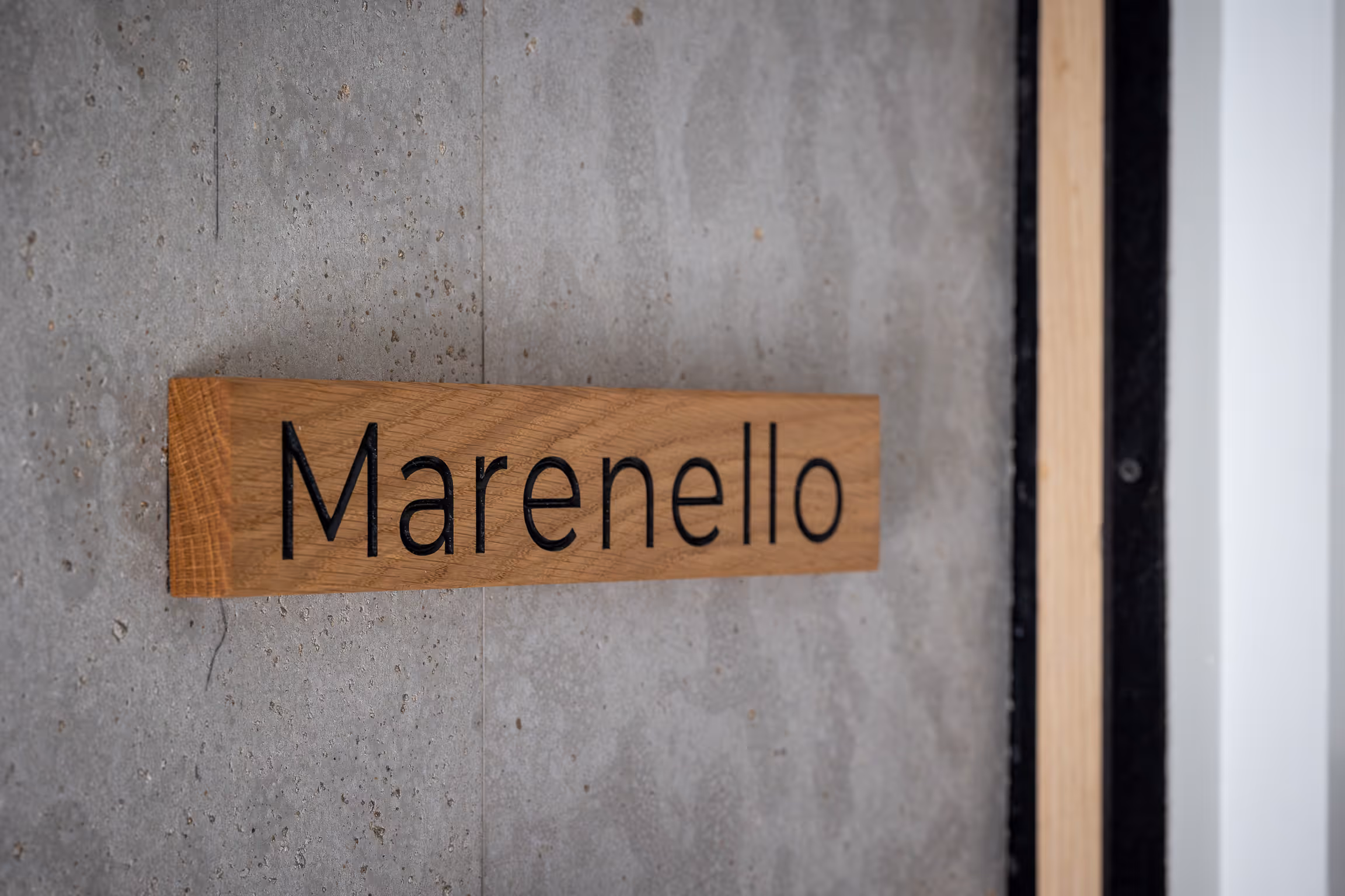 Wooden sign with the word 'Marenello' mounted on a gray concrete wall.